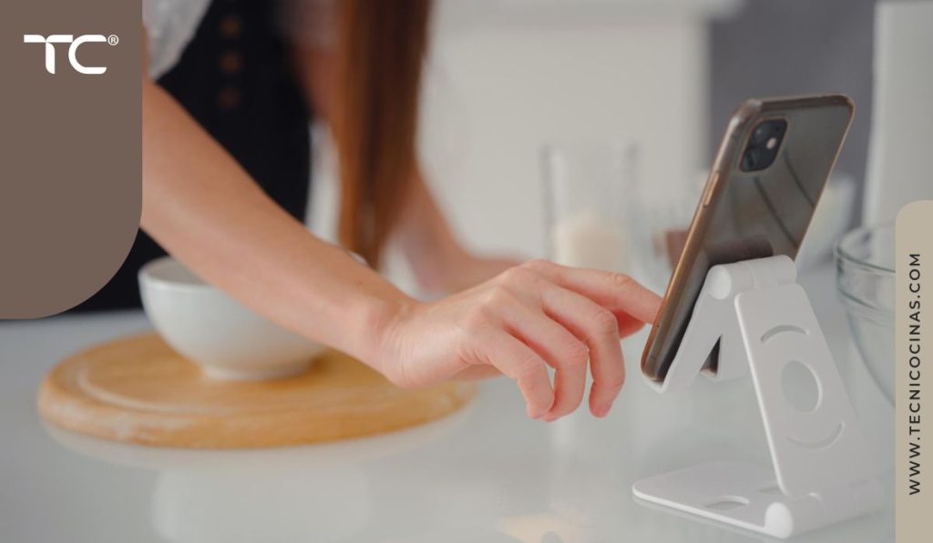 Persona usando celular en soporte mientras prepara alimentos en cocina