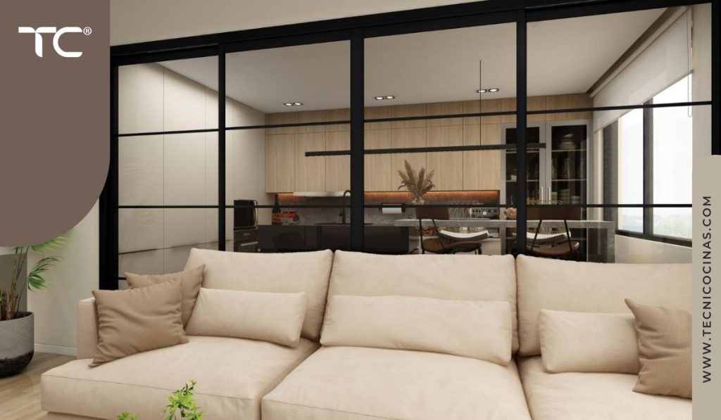 Vista desde la sala a través de cerramiento de cristal transparente con perfiles negros y cocina en madera