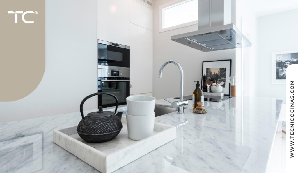 Cocina blanca minimalista con encimera de mármol e iluminación natural suave.