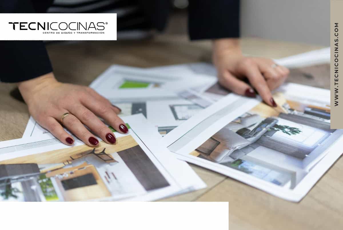 Persona observando imágenes de cocinas sobre una mesa, explorando diferentes estilos y diseños para inspirarse en la renovación de su cocina.