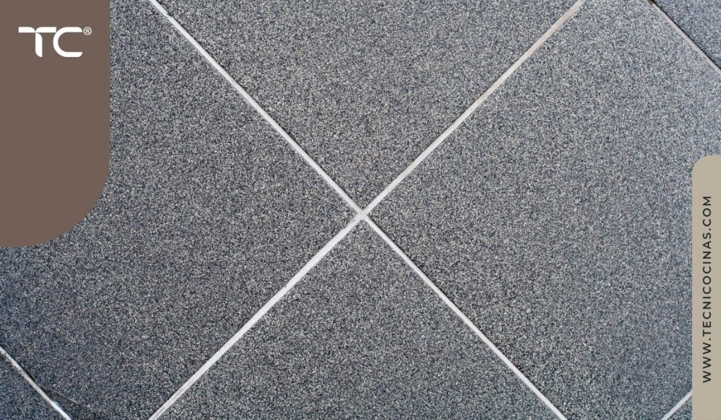 Detalle de piso cerámico con textura granito gris y juntas blancas en cruz, acabado mate antideslizante para cocinas