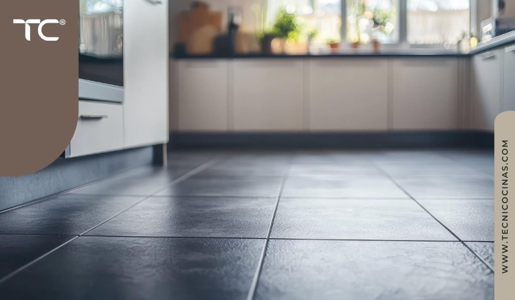 Piso de cocina con baldosas cerámicas grises de gran formato, acabado satinado, gabinetes beige y zona de ventanas con plantas