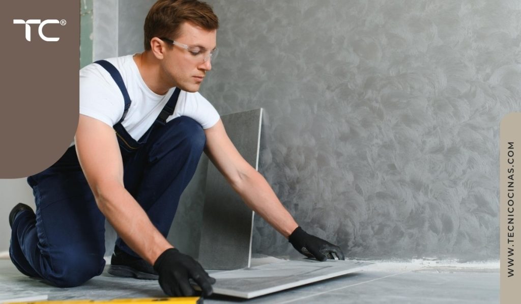 Instalador profesional colocando baldosa cerámica de gran formato sobre piso gris con llana dentada, usando guantes y overol azu